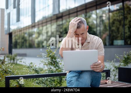 Verärgert, deprimiert reifen grauhaarigen Geschäftsmann mit Hand am Kopf mit Laptop, drahtlose Technologie. Problem und Burnout Stockfoto