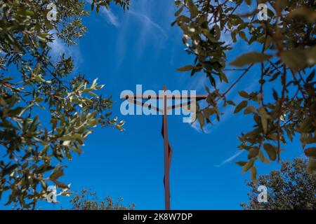 Landschaftlich schöner Blick von den Blättern der Bäume auf das neue hohe Kreuz mit blauem Himmel im Hintergrund. Blick auf Fátima Sanctuary Big Cross Stockfoto