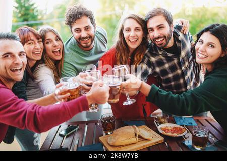 Gruppe von fröhlichen jungen Freunden jubeln mit Wein und Biergläsern bei Picknick-Happy Hour-Party auf der Terrasse - Junge Leute haben Spaß beim Trinken und e Stockfoto