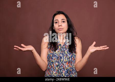 Verwirrt indische Frau zuckt Schultern mit fragenden Gesichtsausdruck Porträt. Verwirrt Dame stehend mit den Händen weit ausgebreitet, zweifelhaft, nachdenkliche Person Blick auf die Kamera Stockfoto