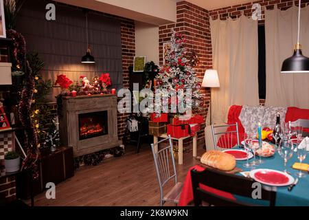 Geschmückter weihnachtsbaum in der Nähe des Kamins, festlicher servierter Tisch, Winterferien traditionelle Vorbereitungen. Weihnachtlicher Dekor im Luxuszimmer, warmes Kerzenlicht am Abend Stockfoto