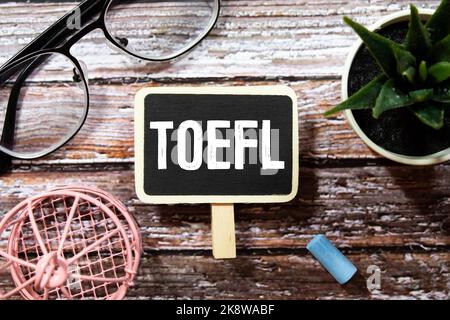TOEFL Englische Testprüfung in schwarzem Notizbuch mit Clips, Markern und Memonotizen auf blauem Tisch geschrieben. Stockfoto