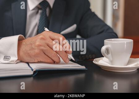 Nahaufnahme der Hände eines Geschäftsmannes, die sich während des Meetings Notizen im Tagebuch machen Stockfoto