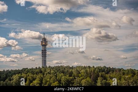 Schweden, Stockholm - 17. Juli 2022: Keksturm, Kaknästornet, Kommunikations- und Sendeturm über grünem Wald unter blauer Wolkenlandschaft Stockfoto