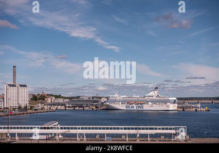 Schweden, Stockholm - 17. Juli 2022: Landschaft, weiß-blaue Silja Line Fähre dockte am Vartaterminalen Terminal im Hafen von Frihamnen unter blauer Wolkenlandschaft an. Stockfoto