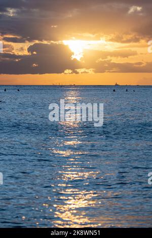 Atemberaubender Sonnenuntergang von Oahu in Hawaii mit Silhouetten von Surfern und Schwimmern. Stockfoto