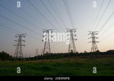 Elektrische Übertragungstürme mit Hochspannungs-Überkopfkabeln direkt über dem Kopf. In einer angenehmen grünen ländlichen Umgebung. Stockfoto