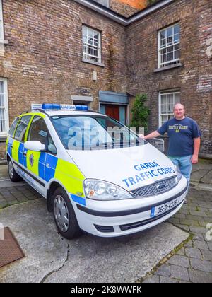 Ein Mann posiert für ein Foto neben einem Garda Traffic Corps Ford Galaxy Minivan Polizeifahrzeug in Dublin, Irland. Stockfoto