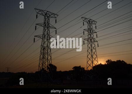 Zwei Strommasten von Electrical Power wurden gegen den goldenen Abendhimmel silhouettiert. In ländlicher Umgebung. Stockfoto