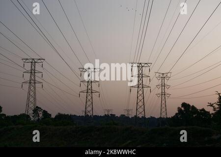 Elektrische Oberleitungen, die von Strommasten mit Kabeln direkt über dem Kopf geführt werden. Silhouetten gegen den Abendhimmel. Marsch in die Ferne. Stockfoto