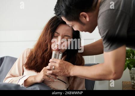 Fürsorglicher Ehemann, der kranke Frau mit einem Glas Wasser versorgt, das an Fieber leidet Stockfoto