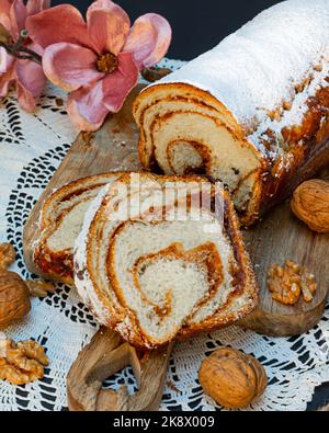 Hausgemachte Zwetschgen- und Walnussstrudel-Nudeln, die mit Puderzucker auf einer Holzbasis mit einer Rose verziert sind. Konzeptionelles Banner für die Gastronomie. Stockfoto