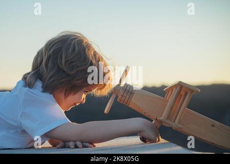 Glückliches Kind spielt mit Spielzeug Flugzeug vor blauem Himmel Hintergrund. Nettes Kind, das an einem sonnigen Sommertag spazieren geht. Kinder träumen vom Reisen. Stockfoto