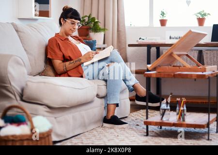 Die Inspiration kommt immer am Wochenende. Eine attraktive junge Frau zeichnet, während sie sich zu Hause auf dem Sofa entspannt. Stockfoto