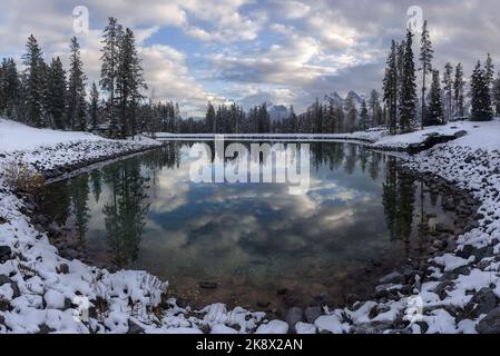 Wolken und Waldbäume spiegeln sich im Canmore Silvertip Golf Course Calm Lake Water wider. Bedeckter Himmel Szenische Herbstlandschaft Kanadische Rocky Mountains Stockfoto