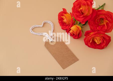 Einfarbige beige Papiernote und Seil in Herzform auf neutralem beigen Hintergrund. Zarte rote Rosen Grußkarte Feiertagsidee. Erstellen Sie einen Kopierplatz für Text. Geschenk Stockfoto