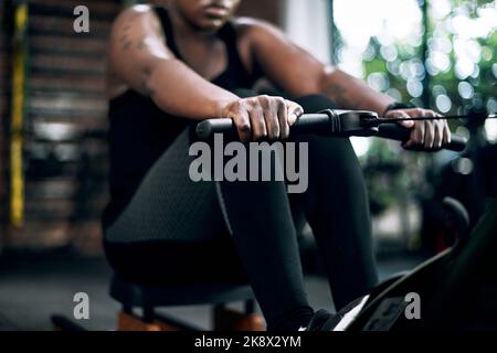 Arbeiten an ihrem Oberkörper. Eine nicht erkennbare junge Sportlerin, die im Fitnessstudio auf einem Rudergerät trainieren kann. Stockfoto