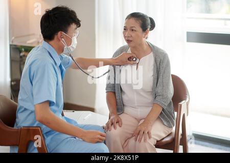 Junger Arzt, der den Lungen des Patienten im Pflegeheim zuhört Stockfoto