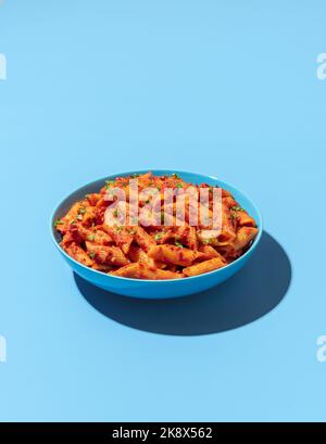 Klassisches italienisches Pastagericht, Penne alla arrabbiata, minimalistisch auf einem blauen Tisch. Penne mit Tomatensauce und Chili auf einem blauen Teller. Stockfoto