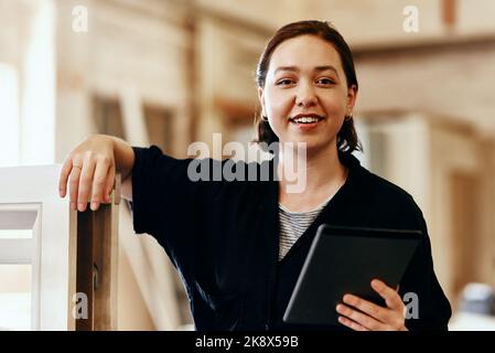 Diese praktischen Apps machen den Designprozess viel einfacher. Porträt einer jungen Zimmermannin, die in ihrer Werkstatt mit einem digitalen Tablet arbeitet. Stockfoto