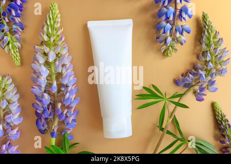 Mockup weiß Kosmetische Tube und Lupinenblüten auf goldgelbem Hintergrund. Creme Feuchtigkeitscreme Hautpflege Produkt blank Kunststoff-Paket. Weiße Flasche mit unb Stockfoto