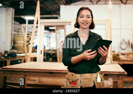 Wir machen Vintage- und Moderne-Stile. Eine Tischlerin mit einem digitalen Tablet in ihrer Werkstatt. Stockfoto