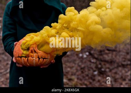 Eine gruselige Hexe hält einen dampfenden Kürbis in einen tiefen Wald. Jack o Laterne strahlt für halloween gelben Rauch aus Stockfoto