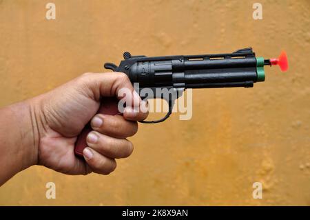 Hand hält Spielzeugpistole auf gelber Wand Hintergrund selektiver Fokus Stockfoto