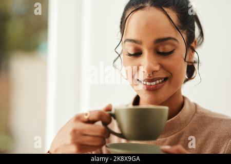 Es gibt nichts Vergleichendes wie den Duft von Kaffee. Eine attraktive junge Frau, die allein in ihrem Haus sitzt und eine Tasse Kaffee genießt. Stockfoto