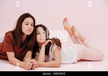 Sich gegenseitig warm anlehnend, zwei Mädchen, die den Bauch nach unten auf den Boden legen Stockfoto