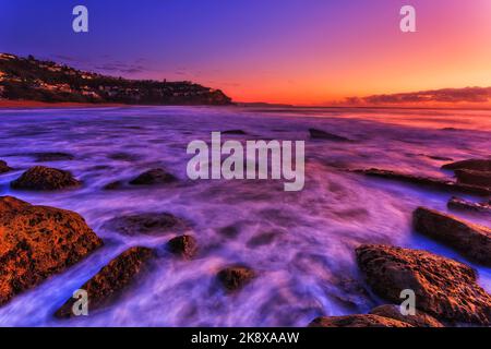 Strahlender, farbenfroher Sonnenaufgang über dem pazifischen Ozeanhorizont am Whale Beach von Sydney Nordstrände mit Blick auf den kleinen Kopf. Stockfoto