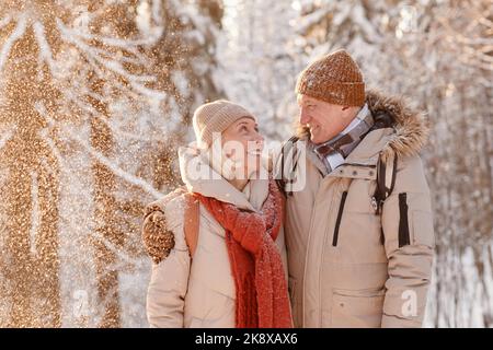 Waist-up-Porträt eines liebevollen älteren Paares umarmt in Winterwald mit Schnee fallen Stockfoto