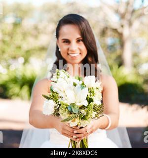 Wie schön sind diese. Beschnittenes Porträt einer schönen jungen Braut, die lächelt, während sie einen Blumenstrauß an ihrem Hochzeitstag hält. Stockfoto