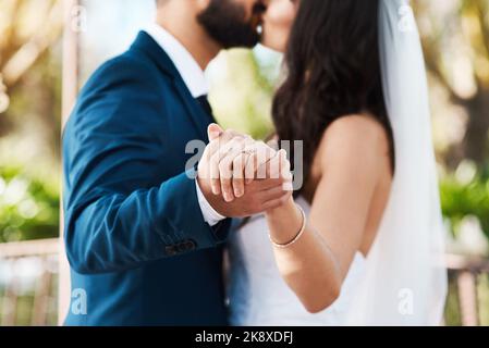 Heute entschieden sie sich für Engagement. Ein unbekanntes frisch verheiratetes Paar küsst sich, während es an ihrem Hochzeitstag die Hände hält. Stockfoto