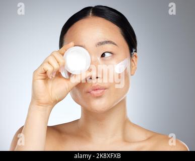 Gesicht, Schönheit und Hautpflege mit einer asiatischen Model-Frau im Studio auf grauem Hintergrund, um ein Produkt zu bewerben. Wellness, Luxus und Gesichtsbehandlung mit einem attraktiven Stockfoto