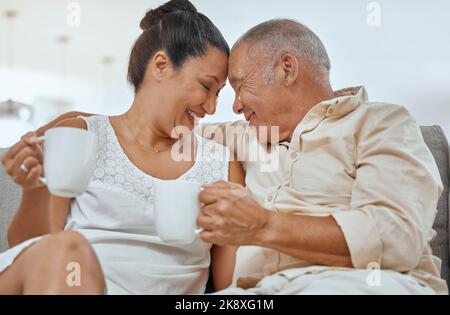 Liebe, Kaffee und ältere Paare entspannen sich auf einem Sofa, trinken Kaffee und umarmen in einem Wohnzimmer. Glückliche Familie, Ruhestand und Tee mit reifen Mann und Stockfoto