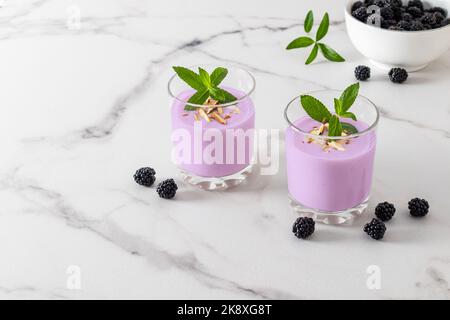 Zwei Gläser mit frisch zubereiteten Bio-Smoothies auf weißem Marmorboden mit Brombeeren. Natürliche Detox. Fruchtdessert Stockfoto