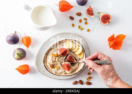 Eine Frau hält einen Löffel mit Haferflocken gefüllt während des Frühstücks. Haferflocken mit Obst in einer Schüssel. Gesunde Ernährung. Entgiftung Stockfoto