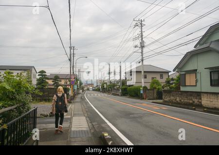 Perspektivischer Blick auf die leere Hauptstraße in einer kleinen Stadt mit Häusern und einem Kabelanschluss entlang der Straße und einem wolkigen blauen Himmelshintergrund. Stockfoto