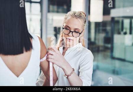 Beim Gestalten geht es um die Details. Eine Modedesignerin nimmt in ihrer Werkstatt Messungen ihrer Kunden vor. Stockfoto