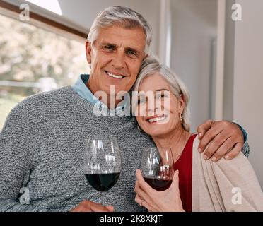 Der beste Wein ist der, der zusammen genossen wird. Ein glückliches reifes Paar, das während eines entspannten Tages zu Hause Rotwein zusammen trinkt. Stockfoto