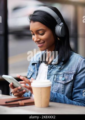Treffen Sie mich zum Kaffee... eine junge Frau, die ihr Mobiltelefon benutzt, während sie Kopfhörer trägt. Stockfoto