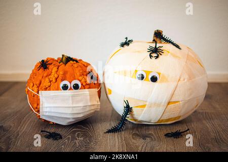 Nahaufnahme von zwei kleinen Kürbissen in Verbänden und in einer Gesichtsmaske mit Würmern und Spinnen auf dem Boden Stockfoto
