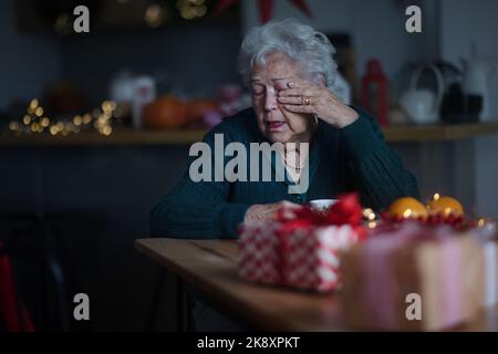 Unglückliche ältere Frau, die allein sitzt und während des Heiligabends weint.Konzept der Einsamkeit Senior und psychische Gesundheit. Stockfoto