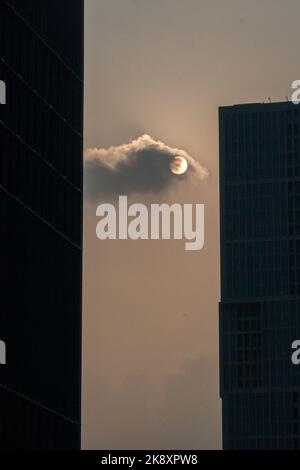 Eine vertikale Aufnahme eines Vollmondes, versteckt hinter den Wolken, die zwischen zwei Silhouetten von Wolkenkratzern zu sehen ist Stockfoto