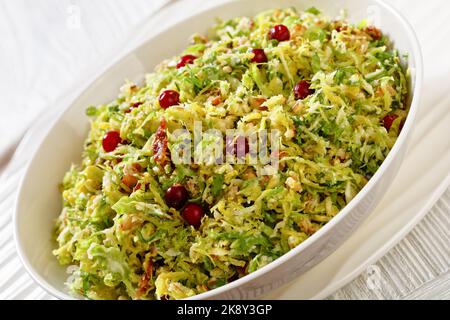 Nahaufnahme von rosenkohl, Mandeln, knusprig gebratenem Speck und Preiselbeeren in einer weißen Schüssel auf einem Holztisch, horizontale Ansicht von oben Stockfoto