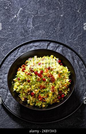 rosenkohl mit Mandeln, knusprig gebratenem Speck und Preiselbeeren in schwarzer Schale auf Betontisch, vertikale Ansicht von oben Stockfoto