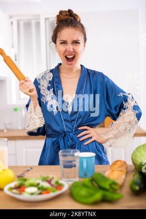 Wütend Frau schreiend und winkend Nudelholz in der Küche zu Hause Stockfoto