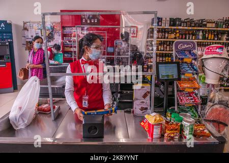 Aufgrund eines Ausbruchs von COVID - 19 trägt ein Kassierer im Supermarkt an einem Kassenschalter einen schützenden Gesichtsschutz. Phnom Penh, Kambodscha. © Kraig Lieb Stockfoto