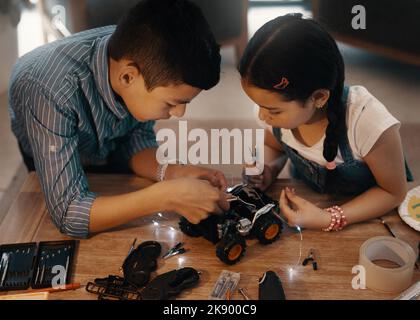 Alles kommt perfekt zusammen. Zwei entzückende junge Geschwister bauen zu Hause zusammen ein Roboterspielzeug. Stockfoto